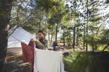Mann hängt Wäsche auf Wäscheleine auf Campingplatz im Wald - CAIF23662