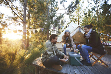 Freunde spielen Karten vor der Jurte auf einem sonnigen Campingplatz im Wald - CAIF23668