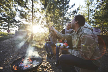 Glückliche Freunde beim Essen auf einem sonnigen Campingplatz im Wald - CAIF23670