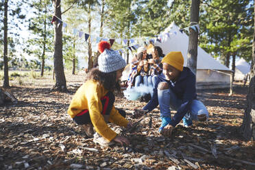 Bruder und Schwester sammeln Brennholz auf einem Campingplatz im Wald - CAIF23671