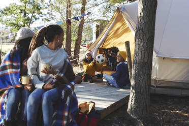 Lesbisches Paar beobachtet Kinder, die mit einem Fußball vor einer Camping-Jurte spielen - CAIF23676