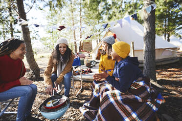 Lesbisches Paar und Kinder kochen Frühstück am Grill auf dem Campingplatz im Wald - CAIF23683