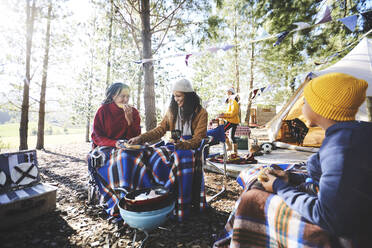 Lesbisches Paar und Kinder essen auf einem sonnigen Campingplatz - CAIF23684