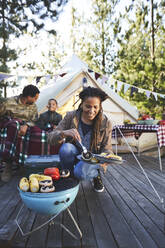 Lächelnde Frau beim Kochen von Gemüse auf einem Grill auf dem Campingplatz - CAIF23685