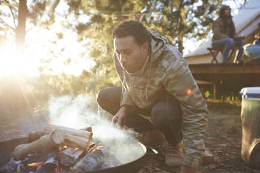 Man blowing on campfire in sunny woods - CAIF23686