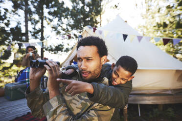 Curious father and son with binoculars at campsite - CAIF23689