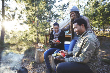 Glückliche Freunde beim Essen auf dem sonnigen Campingplatz - CAIF23691