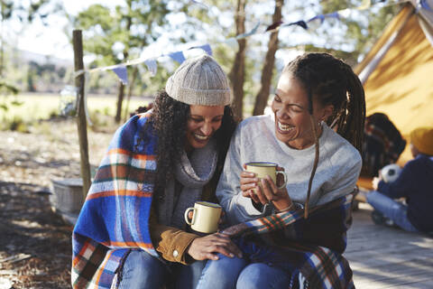 Glückliches, sorgloses lesbisches Paar, das lacht und Kaffee auf dem Campingplatz trinkt, lizenzfreies Stockfoto