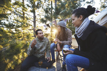 Freunde trinken Wein und unterhalten sich auf einem sonnigen Zeltplatz im Wald - CAIF23695