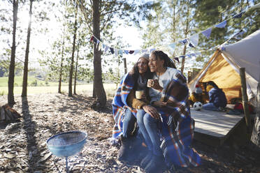 Glückliches lesbisches Paar, das sich auf einem sonnigen Campingplatz im Wald entspannt und Kaffee trinkt - CAIF23701