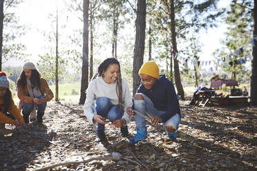 Mutter und Sohn beim Sammeln von Brennholz auf einem Campingplatz in einem sonnigen Wald - CAIF23703