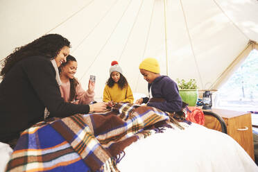Lesbisches Paar und Kinder spielen Karten auf dem Bett in einer Camping-Jurte - CAIF23707