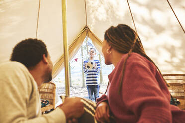 Couple watching son with soccer ball at camping yurt doorway - CAIF23710