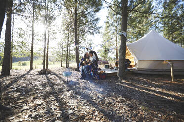 Happy, affectionate lesbian couple relaxing, drinking coffee at sunny campsite in woods - CAIF23711