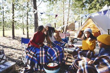 Zärtliches lesbisches Paar mit Kindern küsst sich auf einem sonnigen Campingplatz im Wald - CAIF23713