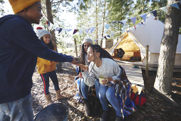 Mutter küsst Laubfrosch in den Händen eines Jungen auf einem Campingplatz im Wald - CAIF23716