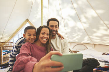 Happy, affectionate family taking selfie in camping yurt - CAIF23719