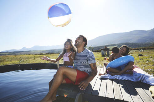 Verspielte Familie mit Strandball im sonnigen Sommerschwimmbad - CAIF23728