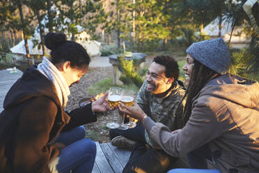 Happy friends toasting wine glasses at campsite in woods - CAIF23731