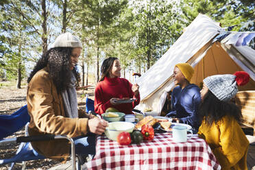 Lesbisches Paar und Kinder essen auf einem sonnigen Campingplatz - CAIF23738