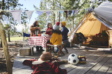 Lesbisches Paar und Kinder essen am Picknicktisch vor der Jurte auf einem sonnigen Campingplatz - CAIF23739