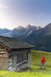 Rückansicht eines Mannes aus einer Steinhütte mit Blick auf den Piz Cengalo und Badile, Tombal, Bergell, Kanton Graubünden, Schweiz, Europa - RHPLF13064