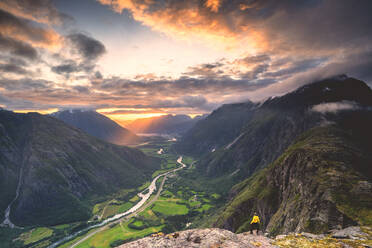 Erhöhte Ansicht eines Mannes, der auf dem Bergrücken Romsdalseggen steht und das Rauma-Tal bei Sonnenuntergang bewundert, Andalsnes, More og Romsdal, Norwegen, Skandinavien, Europa - RHPLF13082
