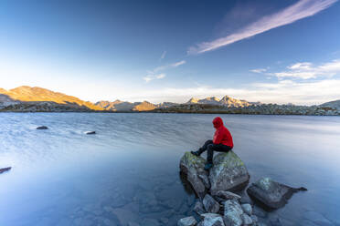 Wanderer sitzt auf Felsen am Ufer der Laghi Azzurri (Bergsee) in der Morgendämmerung, Splugapass, Valle Spluga, Valtellina, Lombardei, Italien, Europa - RHPLF13087