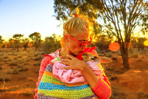 Tourist Frau hält und küsst Känguru Joey bei Sonnenuntergang Licht in Australian Outback, Red Center, Northern Territory, Australien, Pazifik - RHPLF13206
