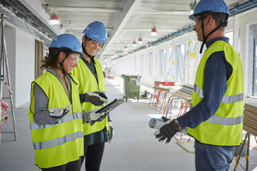 Smiling male and female architects discussing over digital tablet at construction site - MASF15249