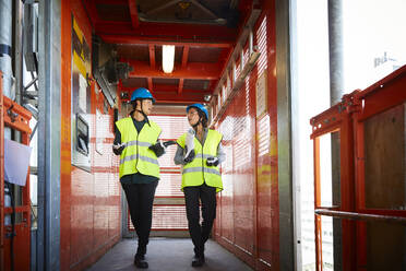 Weibliche Ingenieure diskutieren in voller Länge, während sie in einem Lastenaufzug auf einer Baustelle gehen - MASF15265