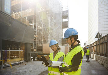 Female engineers discussing over digital tablet at construction site during sunny day - MASF15270