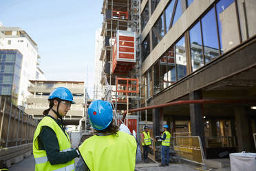 Female architects in reflective clothing discussing at construction site - MASF15271