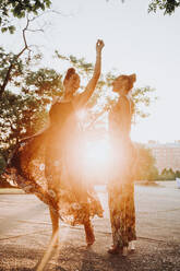 Zwei fröhliche Zwillingsschwestern tanzen bei Sonnenuntergang im Freien - JCMF00330
