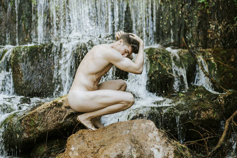 Nackter junger Mann vor einem Wasserfall, lizenzfreies Stockfoto