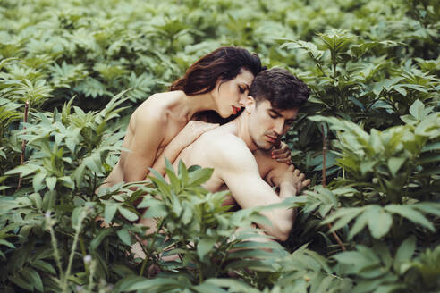 Nude young couple between plants in the forest - MIMFF00040