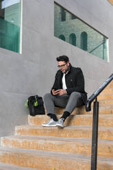 Young man is watching his smartphone on the street - CAVF70483