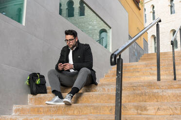 Young man is watching his smartphone on the street - CAVF70484
