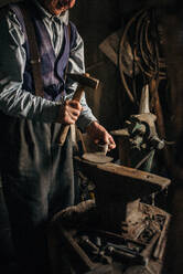 Old man working with hammer in the blacksmith. - CAVF70522