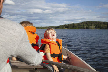 Erwachsener beim Segeln mit aufgeregten Jungen auf einem Boot in einem See, Finnland - CUF53729