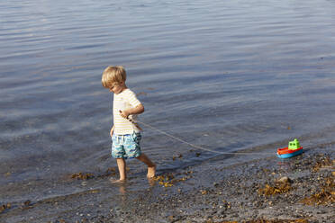 Boy playing with toy boat on beach - CUF53738