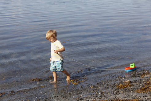 Junge spielt mit Spielzeugboot am Strand - CUF53738