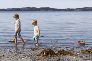 Brüder spielen mit Spielzeugboot am Strand - CUF53739