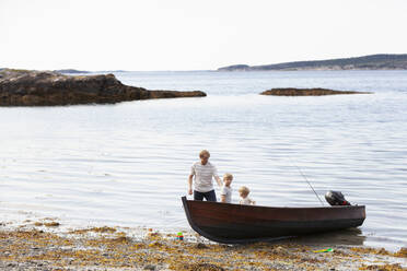 Vater und Söhne spielen neben einem am Strand vertäuten Boot, Norwegen - CUF53741