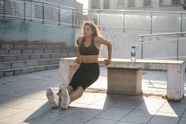 Young woman doing tricep dips on concrete bench - CUF53762