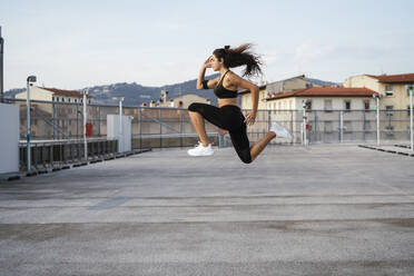 Junge Frau macht hüpfende Ausfallschritte auf einer Dachterrasse - CUF53764