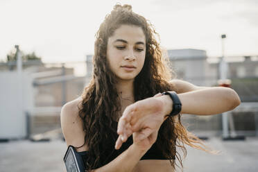 Young woman checking smartwatch on rooftop deck - CUF53768