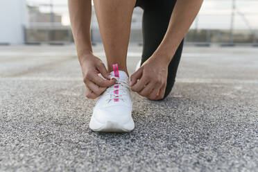 Young woman tying shoelace on rooftop deck - CUF53773