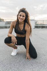 Young woman squatting on rooftop deck - CUF53780