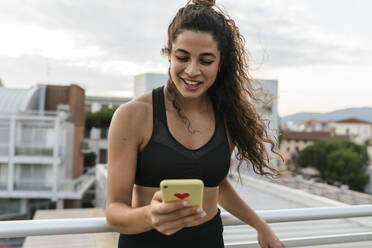 Young woman using smartphone on rooftop deck - CUF53783